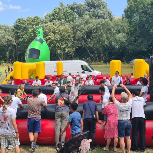 Menschen Kicker Cup. Zwei Felder sind aufgebaut. Mehrere Personen sind auf den Spielfeldern und spielen. Zuschauer säumen die Kickerfelder.