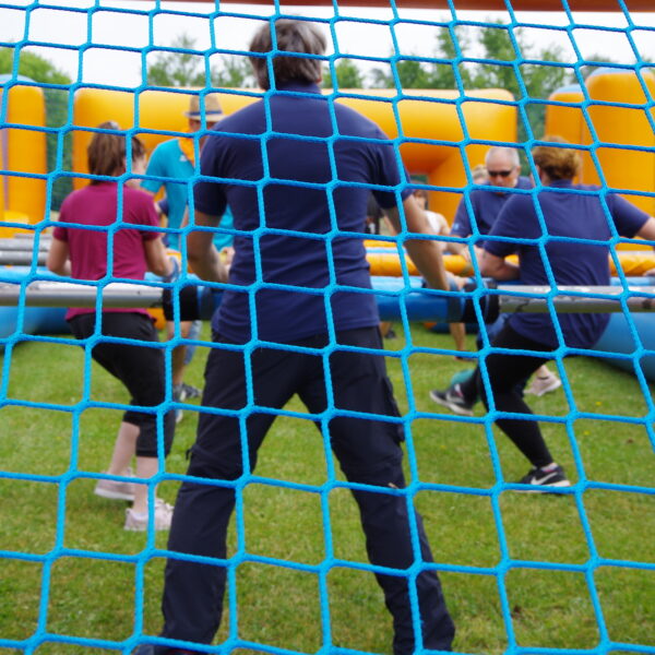 Das Bild zeigt den Torwart und einige Spieler beim Menschen Kicker-Spiel. Das Foto ist durch das Torwartnetz aufgenommen.