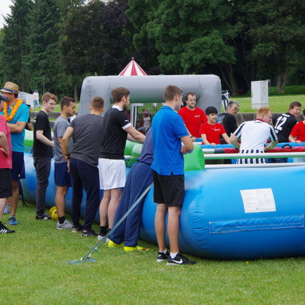 Mehrere Personen stehen um das Fußballfeld, dem sog. Menschenkicker, auf der Seewiese. Der Menschenkicker ähnelt ein wenig einer aufgeblasenen Hüpfburg.