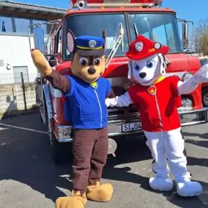 Die beiden Paw Control Maskottchen (zwei Hunde in Polizei und Feuerwehruniform) lassen sich vor einem alten amerikanischen Feuerwehrfahrzeug fotografieren.